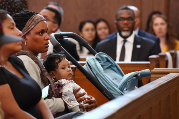 With Chicago mayor Brandon Johnson sitting in the background, Thania Vera holds her 5 month-old baby Yhonector, as the recent migrants from Venezuela listen in to speeches at a ceremony to mark the opening of the St. Bartholomew family shelter in the Portage Park neighborhood on Tuesday, June 11, 2024. (Chris Sweda/Chicago Tribune)