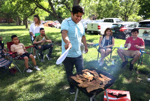 Franklin Guallpa fans away smoke while grilling beef with friends and family in Chicago's Horner Park on Memorial Day on May 27, 2024.  (Chris Sweda/Chicago Tribune)