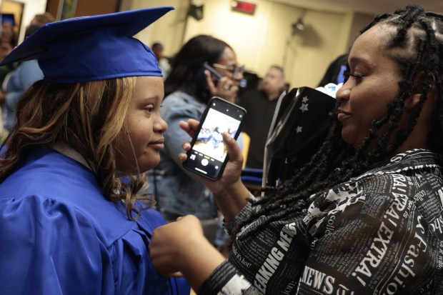 Radisha Walker adjusts her daughter, Heaven Lockhart, graduation robe before she takes a photo of her with her cell phone following Lockhart's graduation ceremony at Lindbloom Math and Science Academy on May 29, 2024, in Chicago. (Antonio Perez/Chicago Tribune)